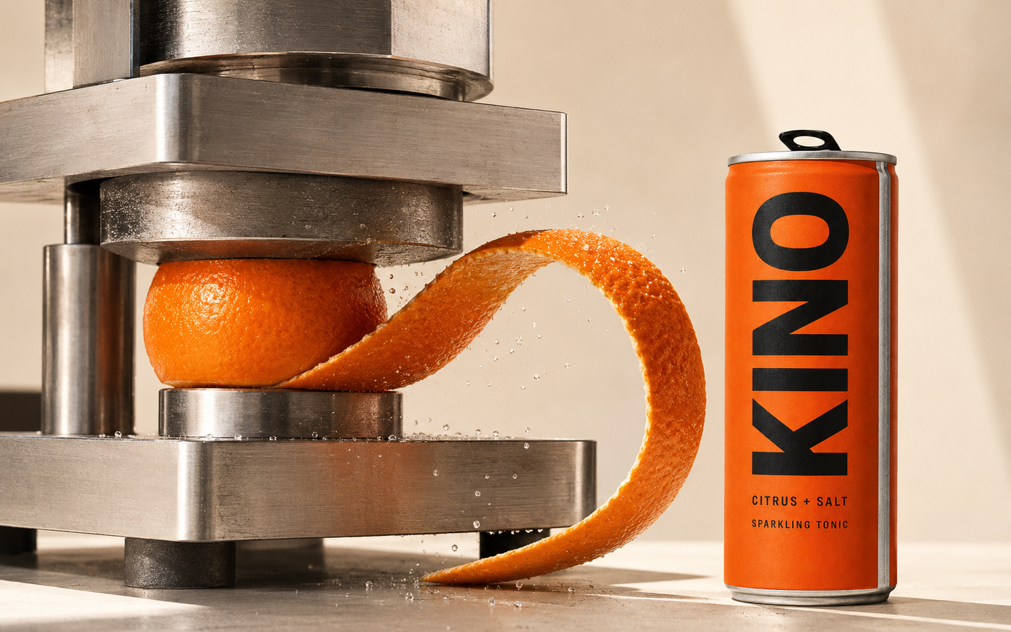 KINO citrus tonic beside a steel press and one sculptural ribbon of kinnow rind